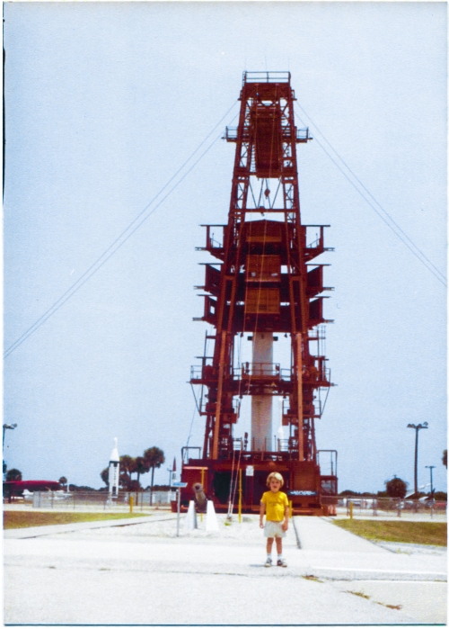 Kai MacLaren, three years of age, stands on one of the concrete pads at the Air Force Space and Missile Museum, Cape Canaveral Air Force Station, Florida. Behind him, viewed from its back side, the red gantry of complex 26 stands in its mated position with a Redstone-derived Juno 1 rocket on its launch stand. Juno 1 was the rocket, and this is the launch pad from which it flew, that placed America’s very first satellite into orbit on January 31, 1958, at the dawning of the “Space Race” with Russia, which culminated in the successful landing of humans on the surface of the Moon on July 20, 1969, and their safe return to Earth afterwards. Photo by James MacLaren.